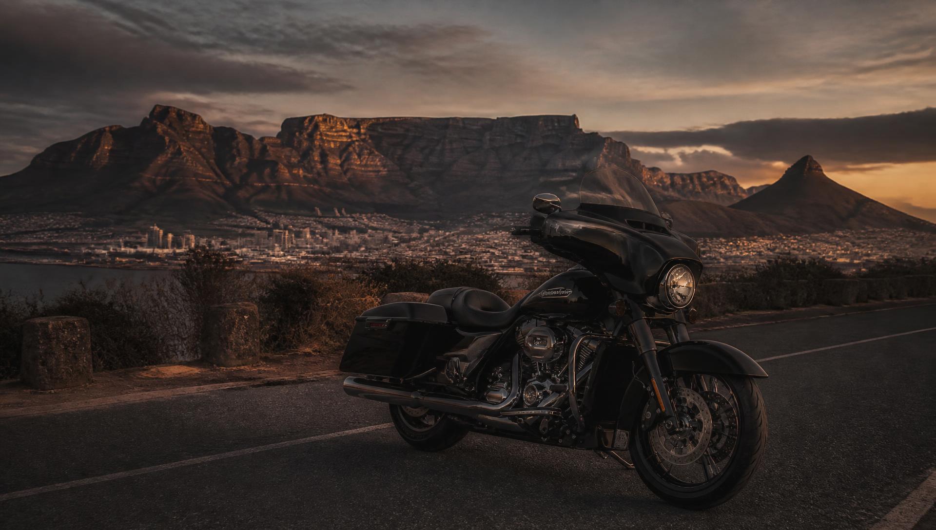 Harley-Davidson touring motorcycle parked with Table Mountain and Cape Town behind it at dusk